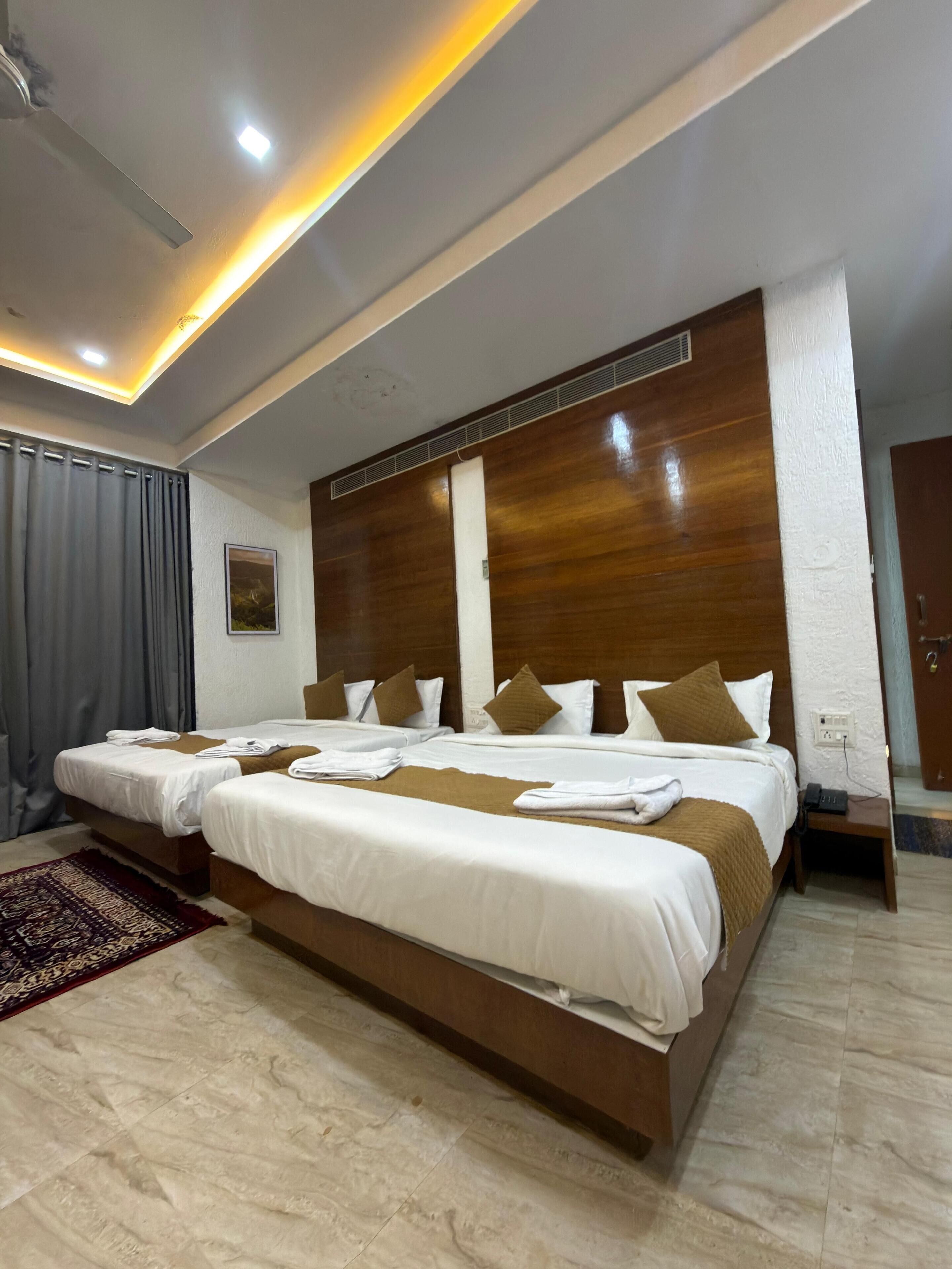 A hotel room with two beds, a large wooden headboard, a marble floor, and a modern ceiling design.