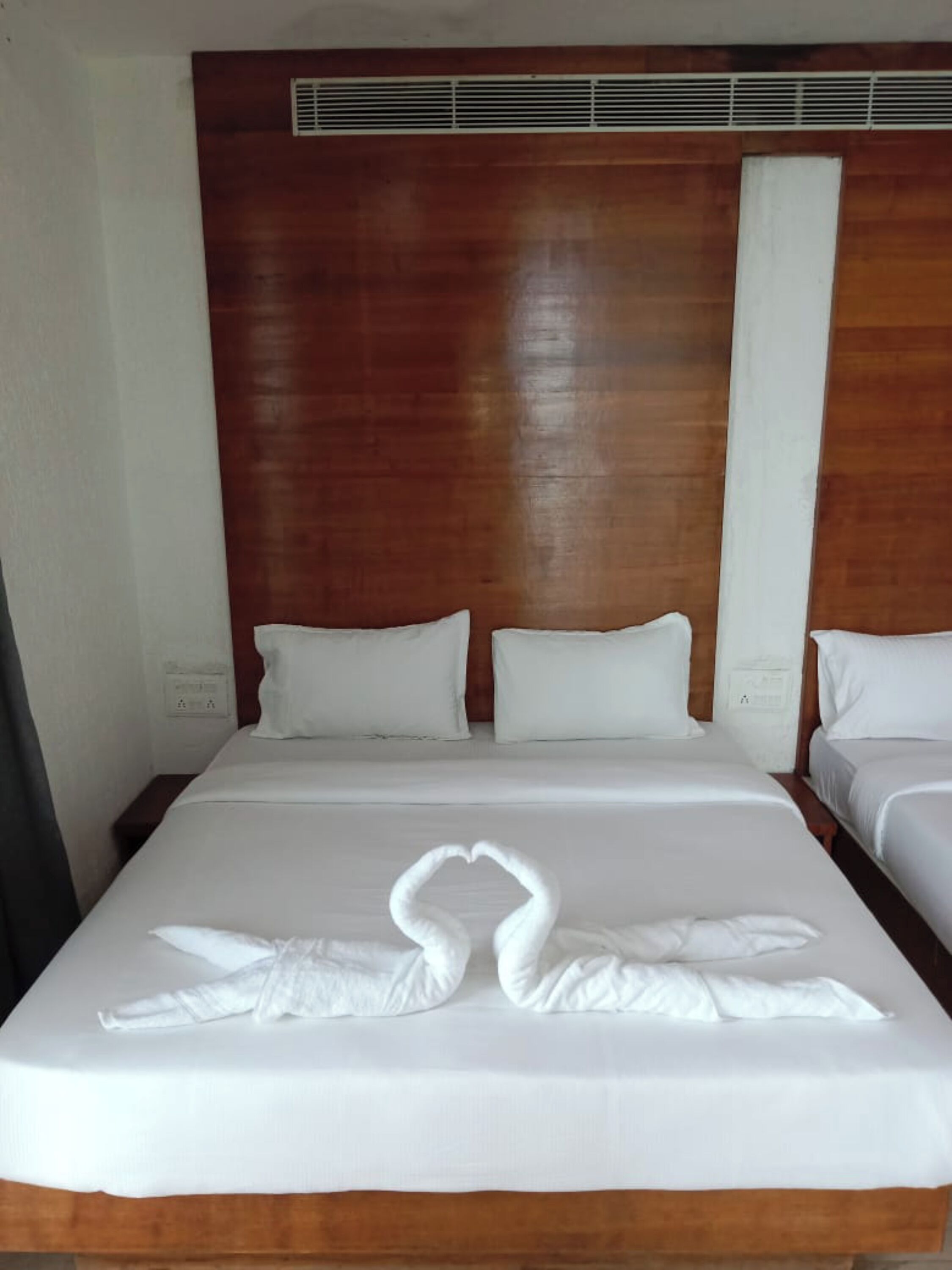 A hotel room with a wooden headboard, two beds, and a decorative swan made of towels on the bed.