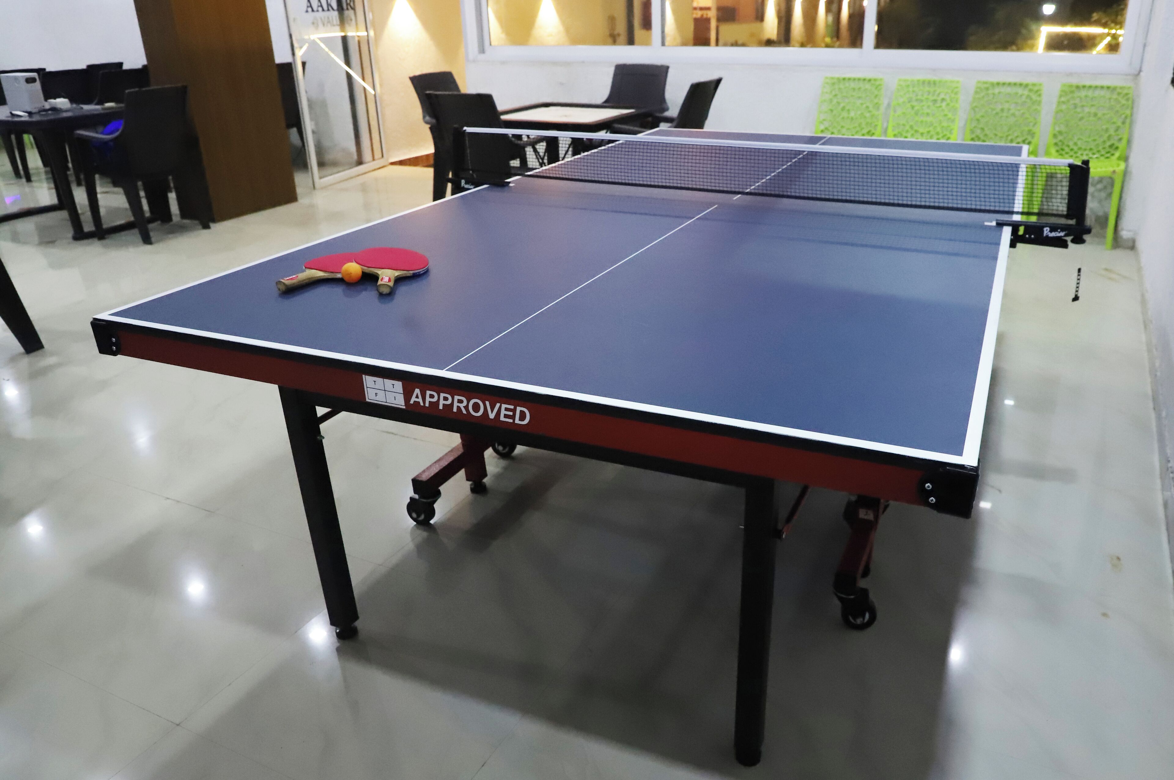 Una mesa de ping pong con estructura roja y negra, una raqueta roja y blanca, y una red.