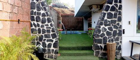 Un patio con un muro de piedra, un pequeño jardín y un vehículo estacionado afuera.