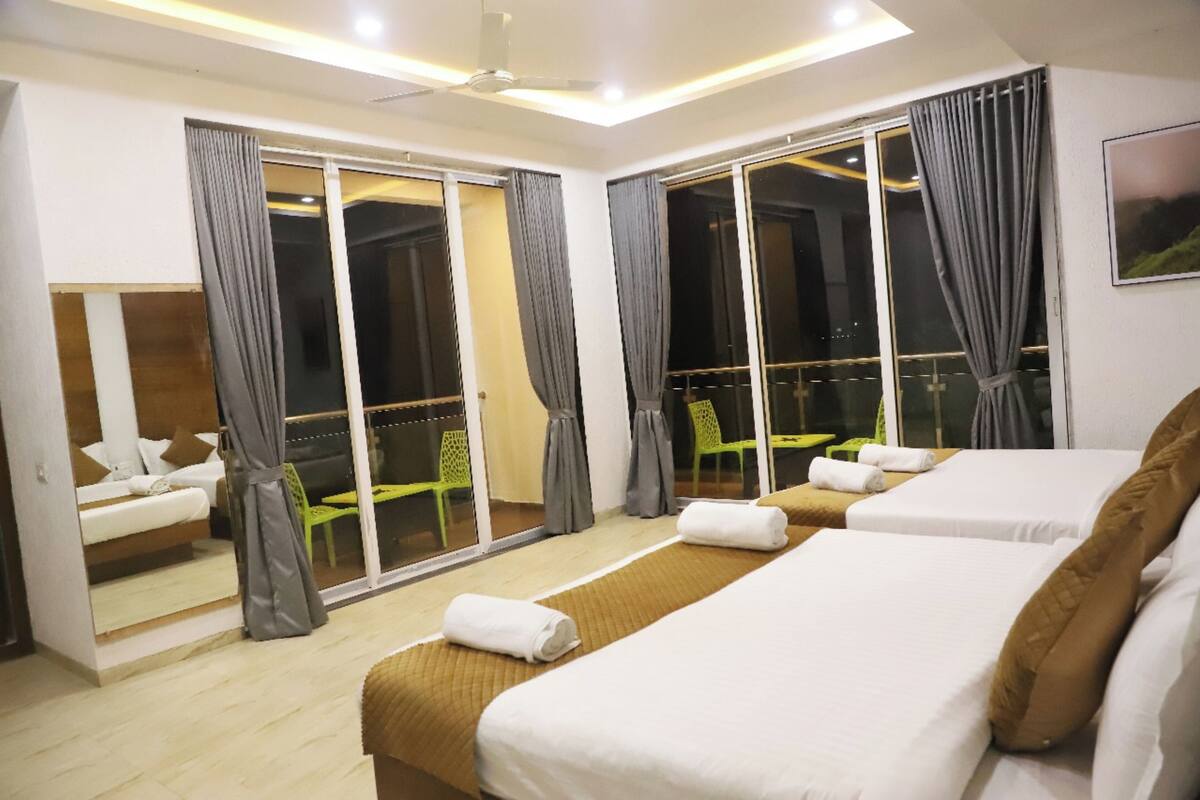 Une chambre d’hôtel dotée d’une grande porte-fenêtre coulissante donnant sur un balcon, d’un lit avec du linge de lit blanc, d’un petit coin salon avec un fauteuil et d’un ventilateur de plafond.