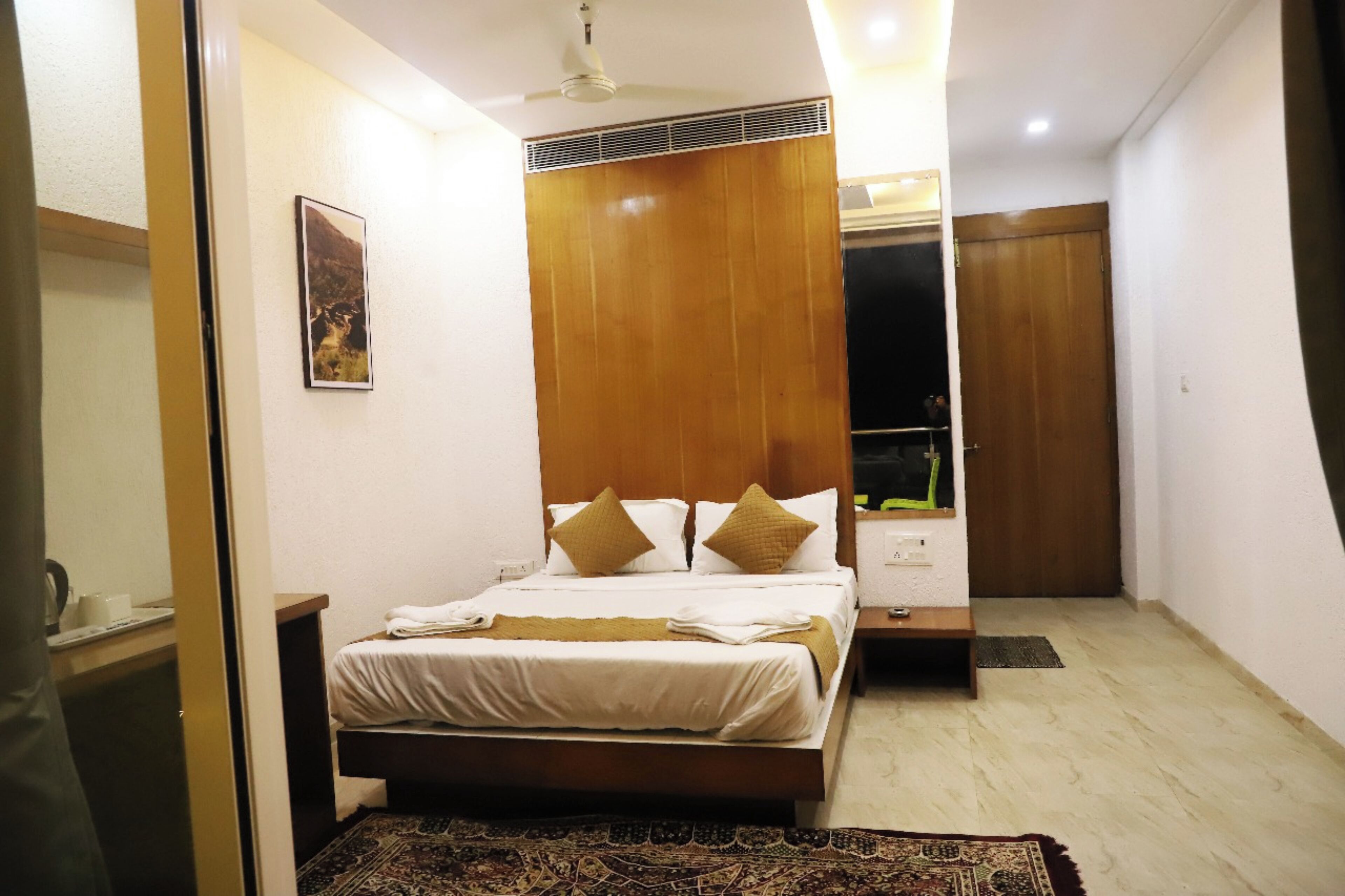 A hotel room with a bed, bedside table, nightstand, and a mirror.