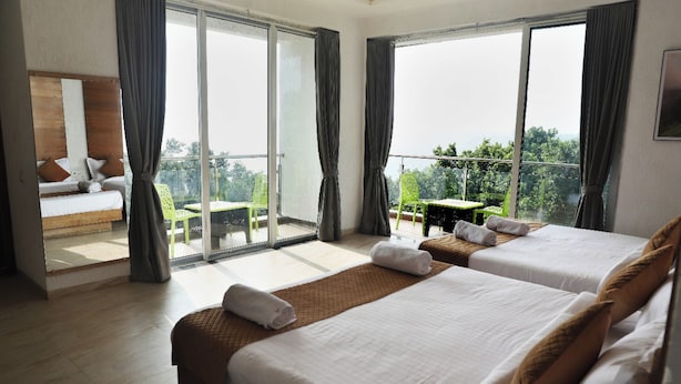 A hotel room with two beds, a balcony with a table and chairs, and a view of the outdoors.