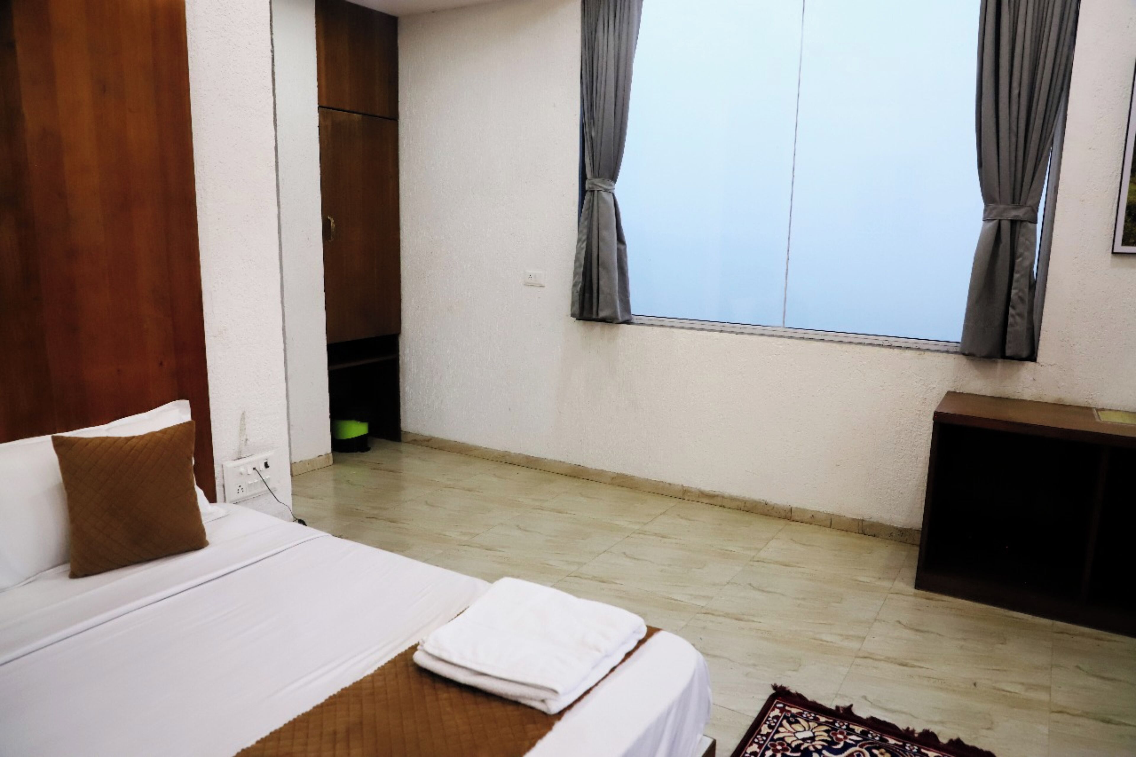 Una habitación de hotel con cama, una mesita, una ventana con cortinas y un armario de madera.