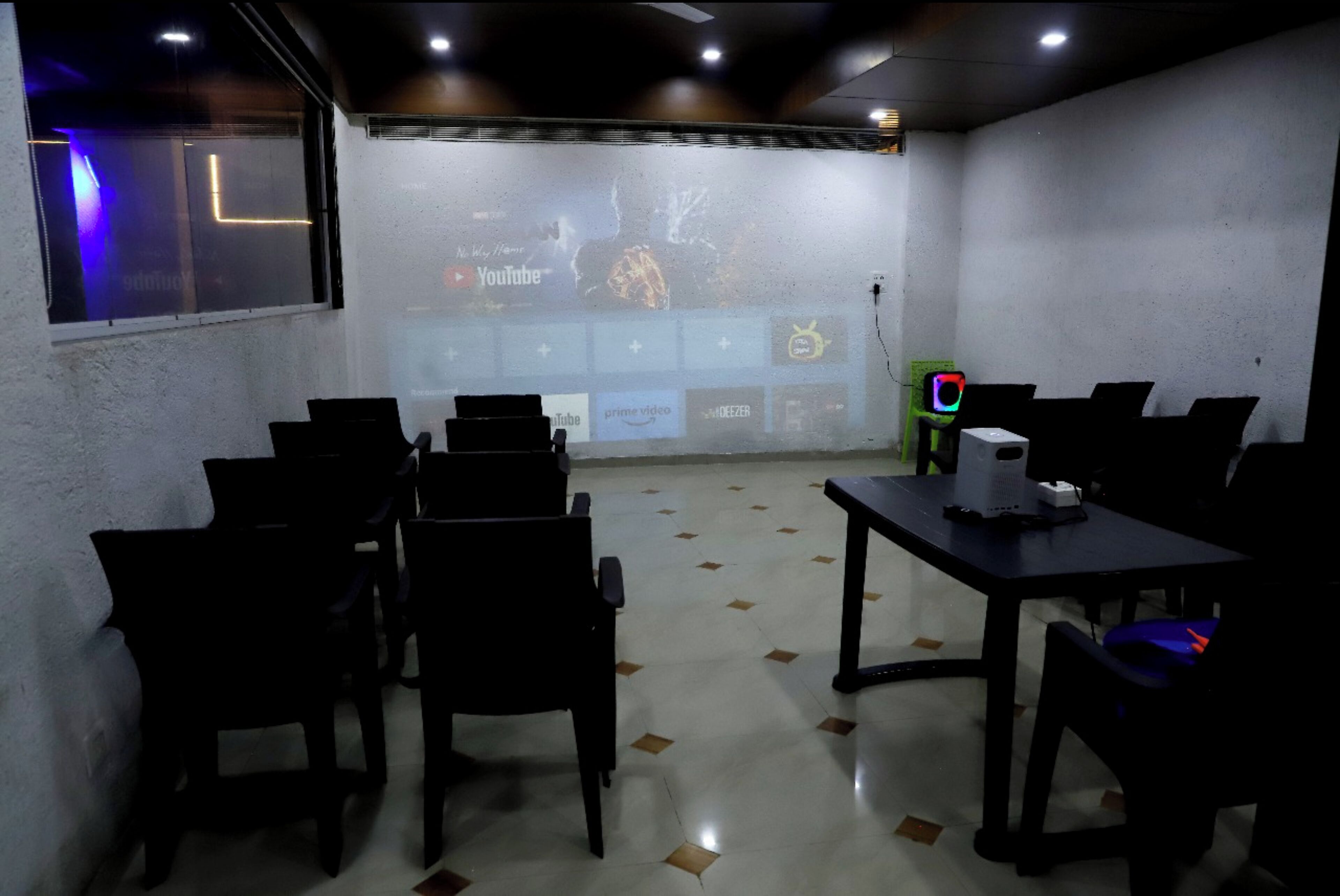 A conference room with a projector screen displaying a presentation, a table with a laptop, and several chairs arranged around the table.
