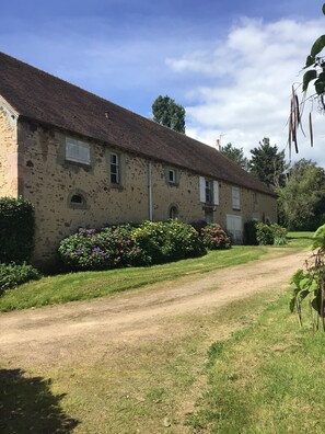 A rustic stone building with a dirt path leading to it, surrounded by lush greenery and flowering plants. - Large house with breathtaking views of an 18-hole golf course and the Cher valley (Nassigny)