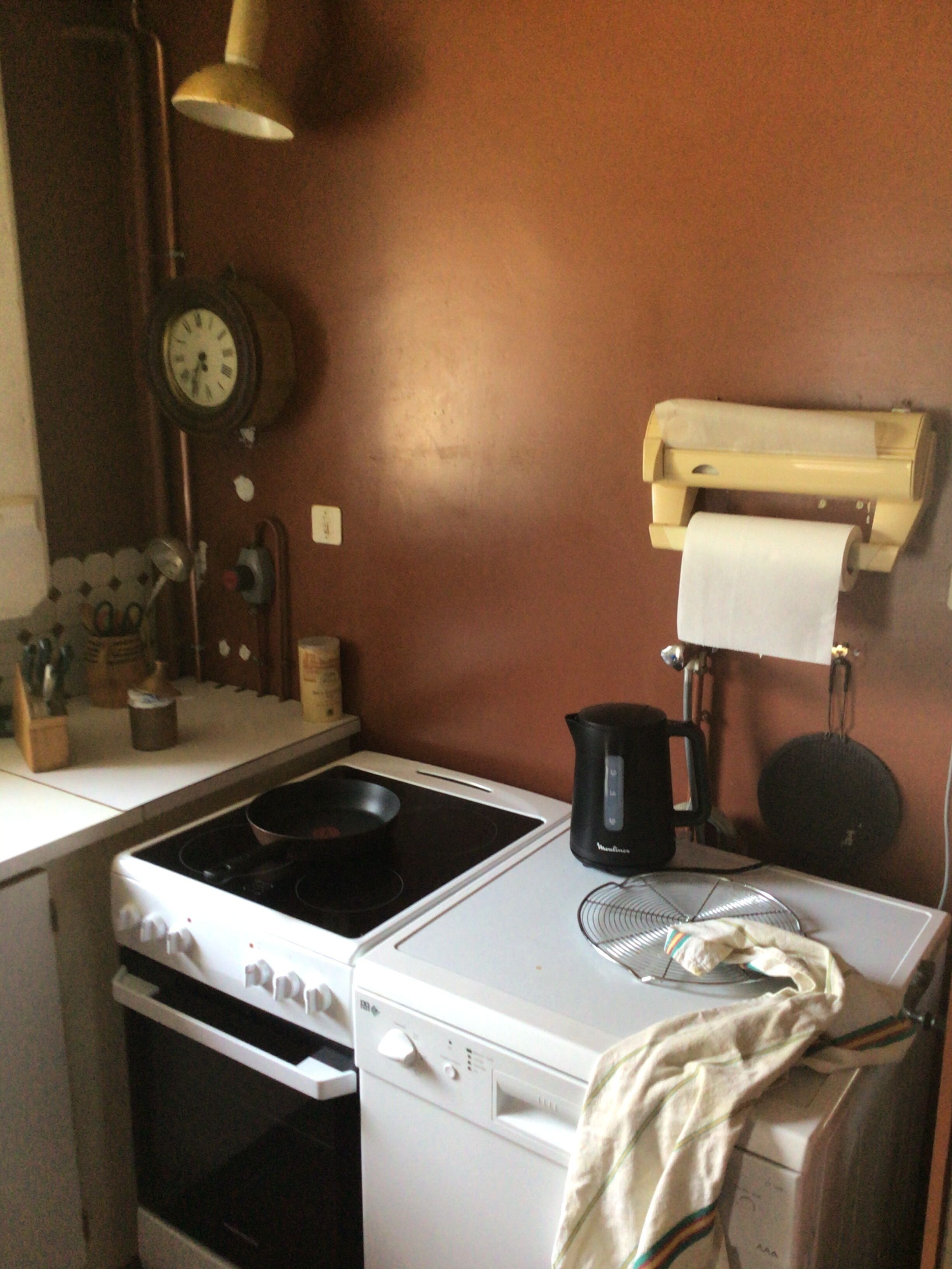 Une cuisine compacte équipée d’une cuisinière, d’un four et d’un lave-vaisselle. Une horloge et un distributeur d’essuie-tout sont fixés au mur.