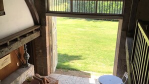 Een patio met een stenen vloer, een ronde tafel met stoelen, rieten meubels en uitzicht op een groen gazon door een open deur.