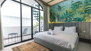 Une chambre moderne avec un grand lit, une fresque murale aux motifs tropicaux, un escalier et un balcon avec des chaises.