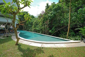A swimming pool surrounded by lush greenery, with a clear sky above. - Greenforest Anahata 4 Star Hotel (Tumbak Bayuh)