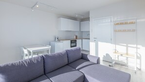 A modern, minimalist living room with a grey sofa, a white dining table, and a kitchen area with white cabinets and a wooden countertop. - Modern, Renovated Studio With Open Views (Middelkerke)