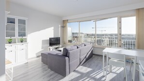 A modern living room with a grey sofa, a white TV stand, and a dining table. - Modern, Renovated Studio With Open Views (Middelkerke)