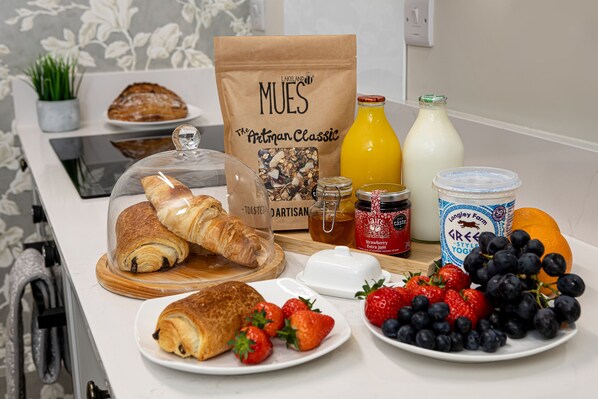 Desayuno con cruasanes, fresas, arándanos, una botella de jugo de naranja, un frasco de mermelada y pan de Mues.