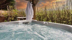 Un jacuzzi con una pérgola de madera sobre él, rodeado de vegetación y vistas a un campo.