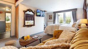 Habitación de hotel con cama, sofá, televisor, zona de comedor y ventana con cortinas.