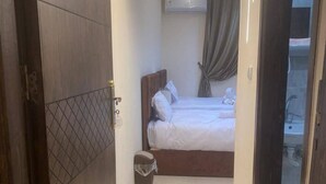 Une chambre d’hôtel avec un lit, une petite poubelle et une porte donnant sur une autre pièce.
