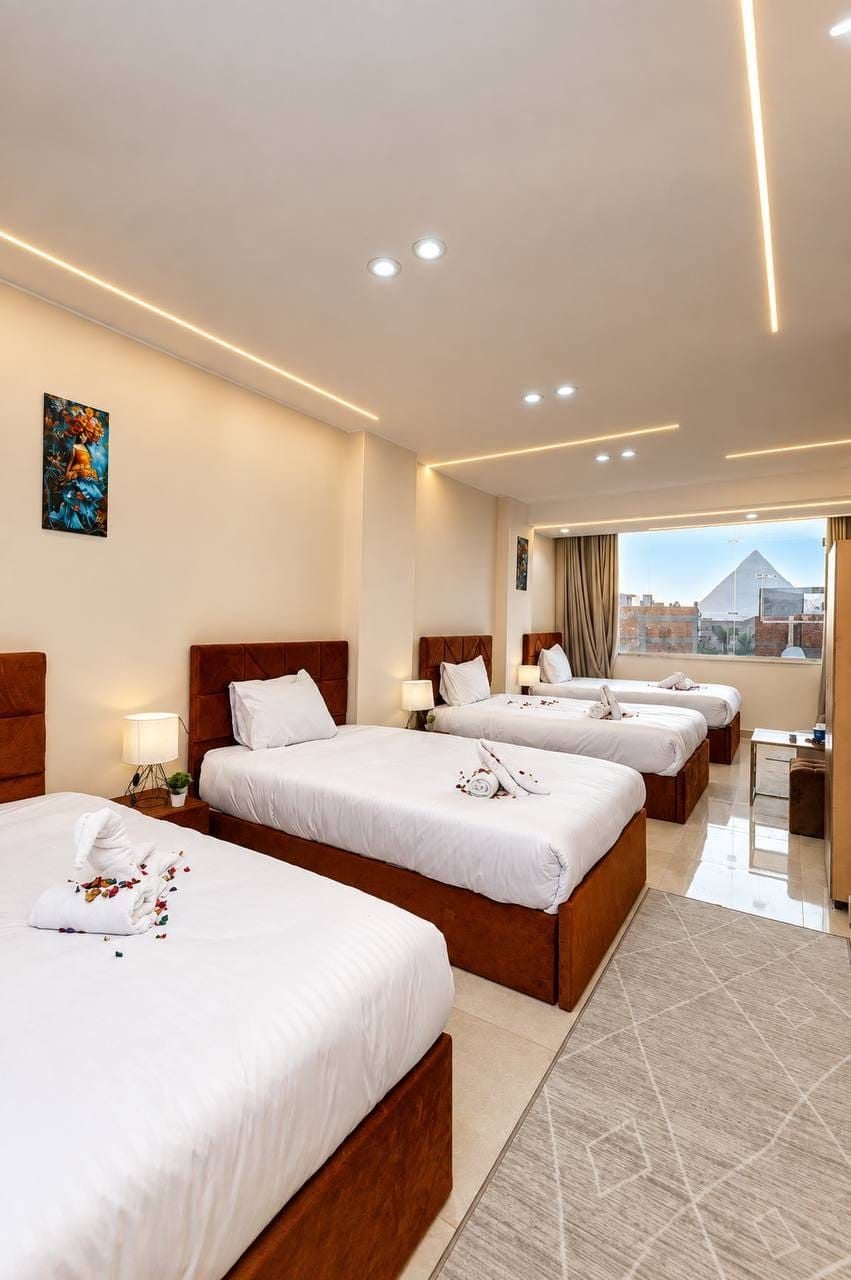 A hotel room with four beds, a desk, and a large window with a city view.