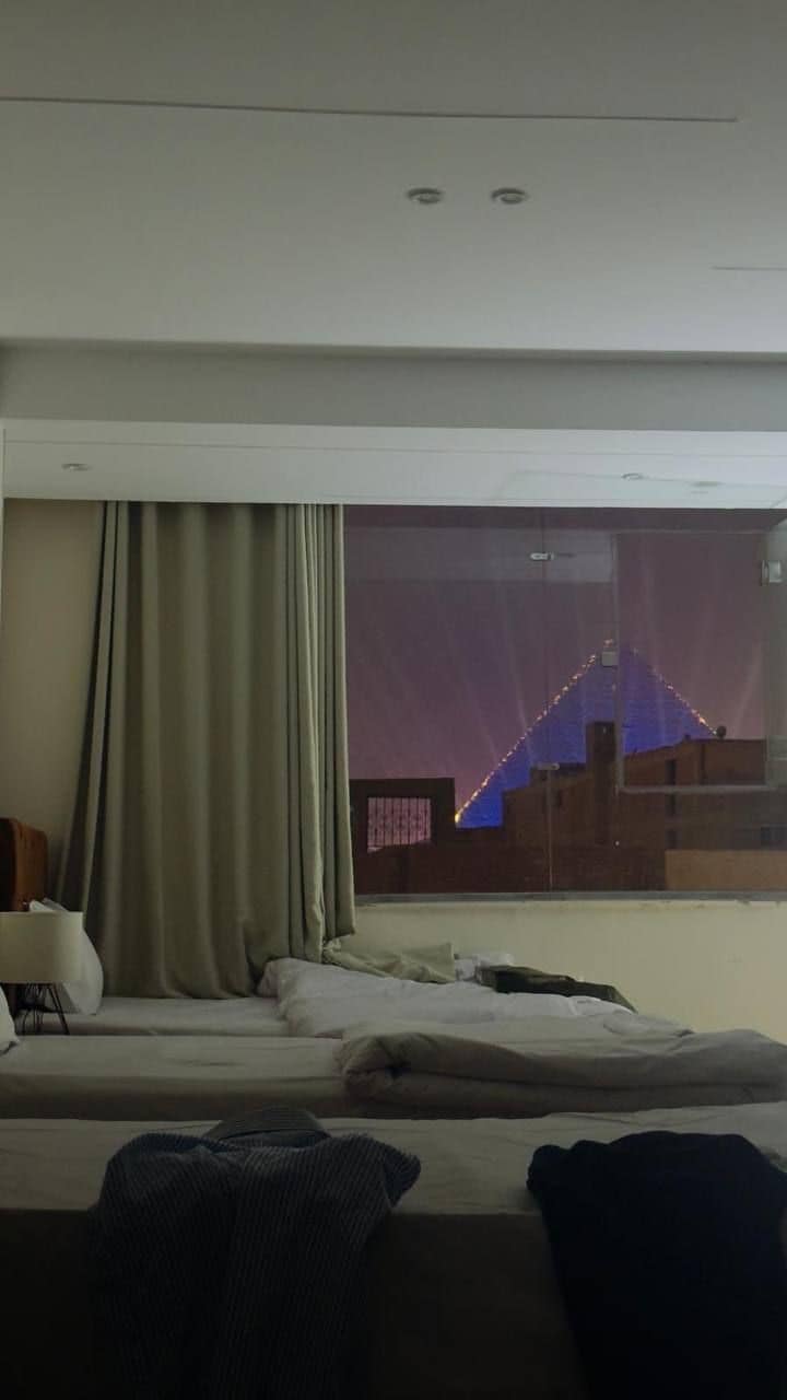 A hotel room with a large window, a bed, a bedside table, and a curtain.