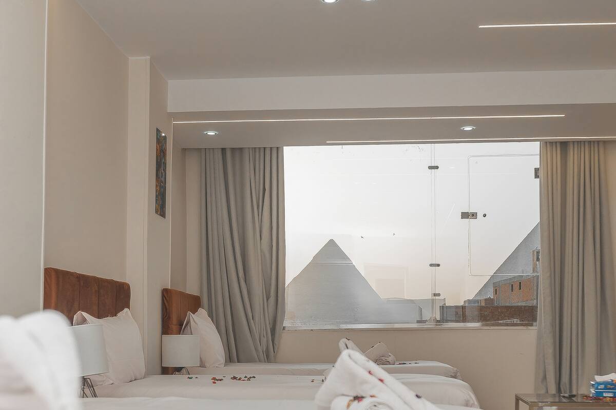 Une chambre d’hôtel avec un grand lit, une table de chevet, une fenêtre avec des rideaux et une vue sur les bâtiments environnants.