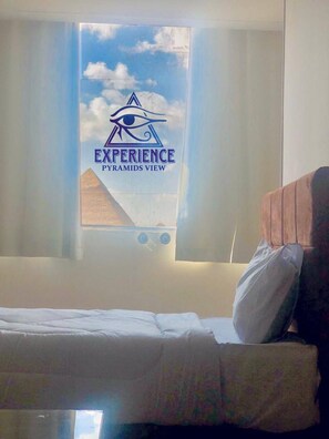 A hotel room with a bed, a window with curtains, and a poster of the Eye of Providence on the wall. - Experieance Pyramids VIEW (Giza)