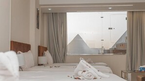 Une chambre d’hôtel avec un grand lit, une vue sur les pyramides et une fenêtre avec des rideaux.