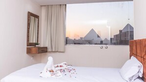 Une chambre d’hôtel avec un lit, une fenêtre donnant sur le paysage urbain, un miroir et une table de chevet en bois.