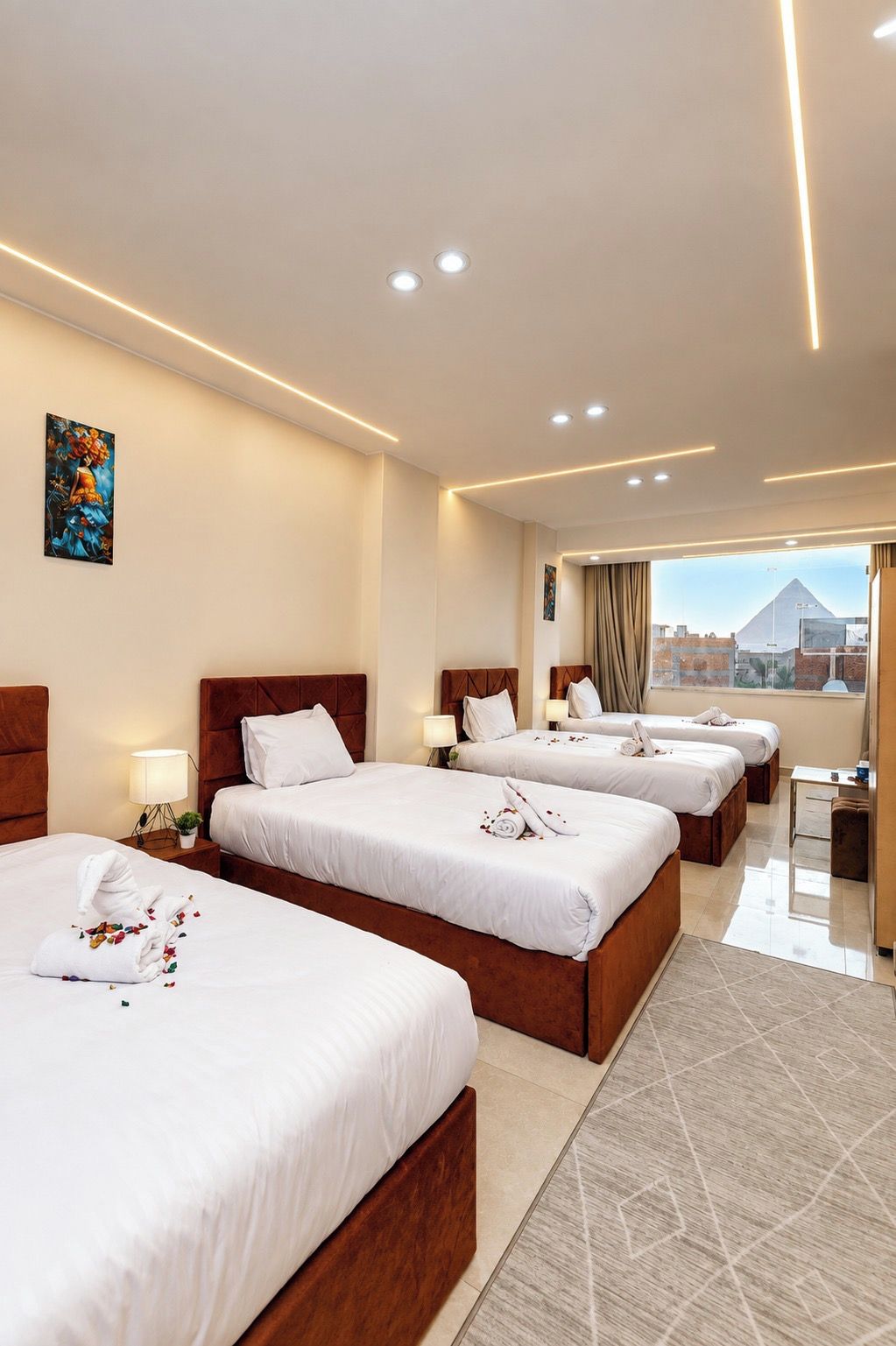 A hotel room with three beds, a desk, and a view of a pyramid.
