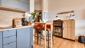 Een moderne keuken met grijze kastjes, een houten aanrecht, een koffieapparaat en twee oranje barkrukken.