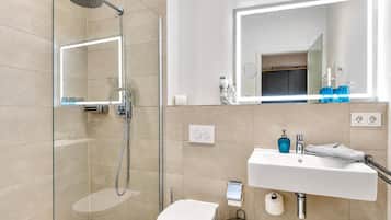 Ein modernes Badezimmer mit einer Duschkabine aus Glas, einem weißen Waschbecken mit Spiegel darüber und einer Toilette.