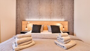 Ein ordentlich bezogenes Bett mit karierter Bettwäsche, zwei schwarzen Kissen und einem Kopfteil aus Holz.