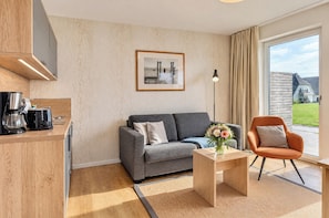 Un salon moderne avec un canapé gris, une table basse et un fauteuil. Un tableau encadré est accroché au mur, et une lampe sur pied se trouve dans un coin de la pièce.