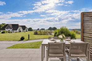 Een terras met een tafel voor twee personen, met uitzicht op een grasveld en een huis.