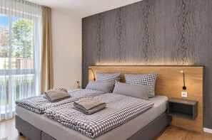 A modern bedroom with a large bed, checkered bedding, a wooden headboard, and a bedside table. - Vacation apartment in the Wreecher Idyll on Lake Wreechen (Putbus)