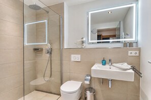 A modern bathroom with a glass-enclosed shower, a white toilet, a sink with a blue soap dispenser, and a mirror with integrated lighting. - Vacation apartment in the Wreecher Idyll on Lake Wreechen (Putbus)