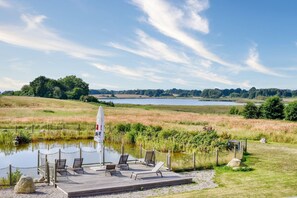 A deck with lounge chairs and a flag, overlooking a lake and grassy fields.
