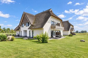 Een modern huis met twee verdiepingen, een groot gazon en een rieten dak.