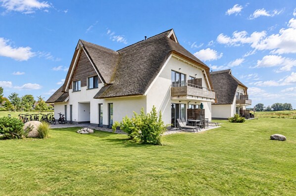 A modern two-story house with a large lawn and a thatched roof.