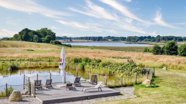 A deck with chairs and a table overlooking a lake, surrounded by a fence and grassy areas. - Vacation apartment in the Wreecher Idyll on Lake Wreechen (Putbus)