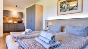 Habitación de hotel con cama, mesita de noche, cabecero, un cuadro enmarcado en la pared y una kitchenette.
