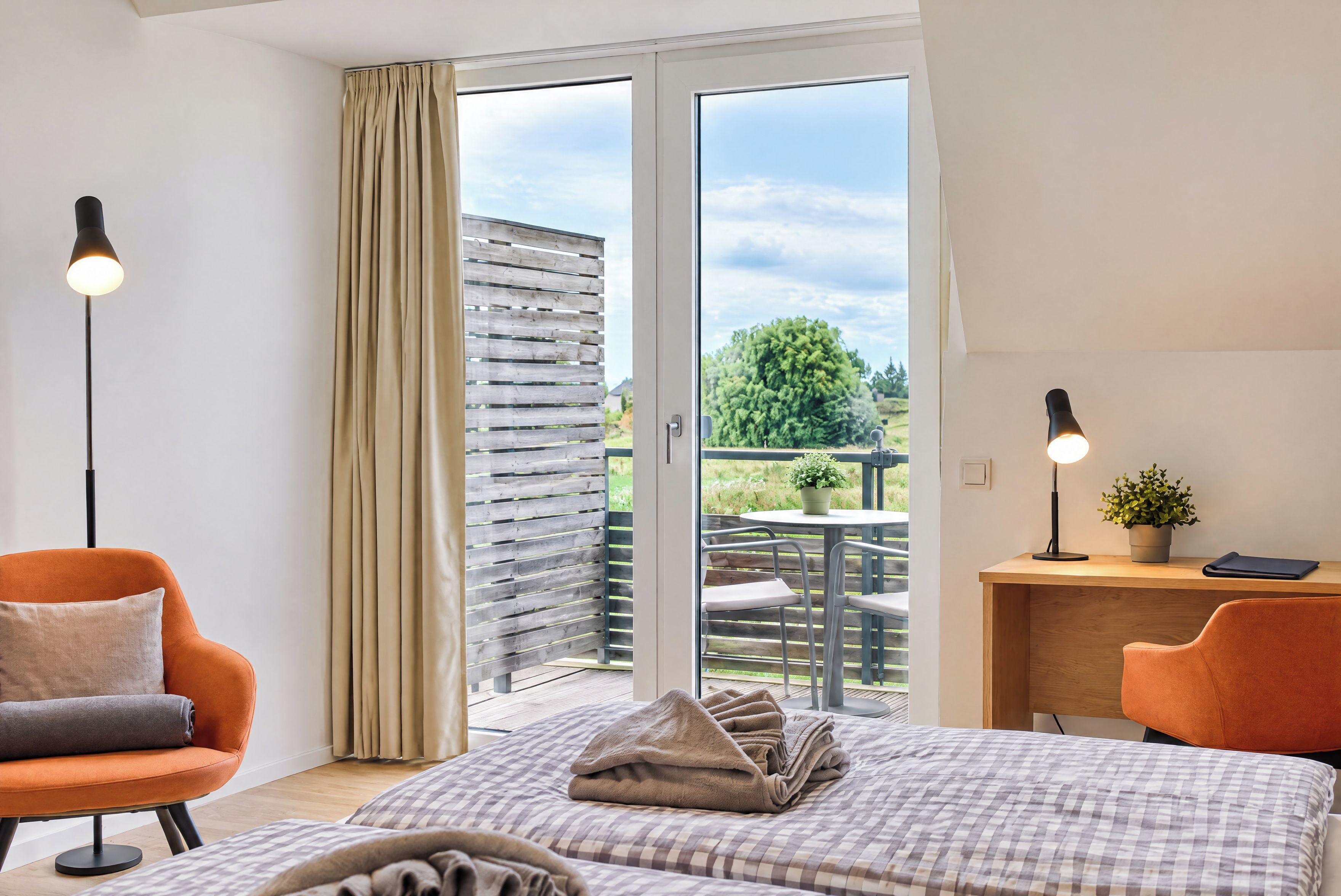 Une chambre d’hôtel avec un lit, deux chaises, un bureau, une plante en pot et une vue sur l’extérieur.