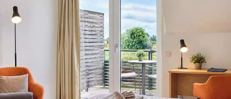 Hotelkamer met een bed, twee stoelen, een bureau, een potplant en uitzicht op het landschap.