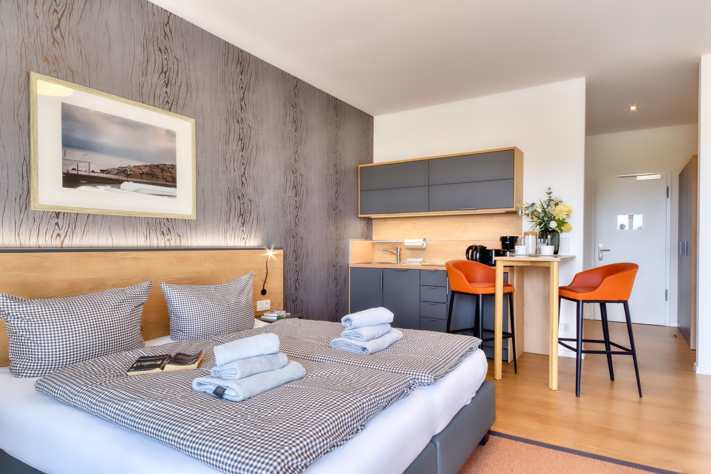 A modern hotel room with a large bed, a desk, and a kitchenette.