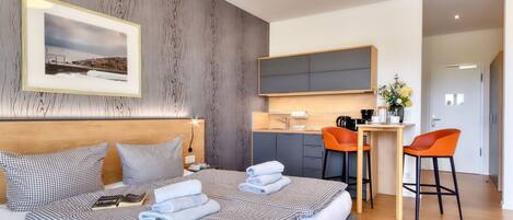 A modern hotel room with a large bed, a desk, and a kitchenette.