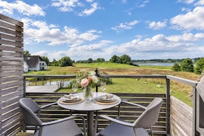 A terrace with a table set for two, overlooking a grassy landscape and a body of water.