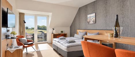 A modern bedroom with a bed, a desk, a chair, a TV, and a balcony with a view.