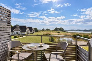Een balkon met een tafel en stoelen, met uitzicht op een grasveld en een waterpartij.