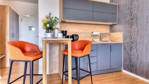 Une cuisine moderne avec deux tabourets de bar orange, une table en bois et un meuble gris placé au-dessus du comptoir.