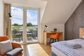 A bedroom with a bed, a desk, and a chair, with a view of a green landscape through a glass door.