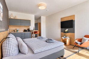Een moderne hotelkamer met een bed, een bureau, een stoel, een televisie en een kitchenette.