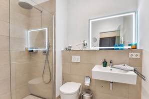 Een moderne badkamer met douche, toilet, wastafel en een spiegel met ingebouwde verlichting.
